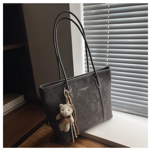 Detail of grey suede tote bag with leather logo and cute plush bear accessory