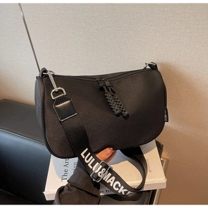 Detail view of black nylon half-moon bag featuring wide lettered strap and woven logo label