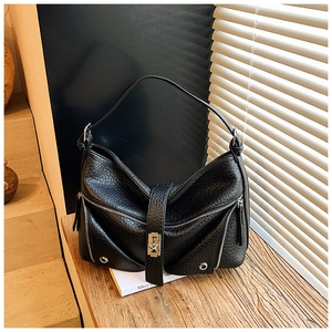 Close-up of black leather tote bag featuring metal zippers and buckle on wooden desk