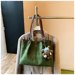 Detail of dark green quilted tote bag with brown leather handles and a plush bear charm