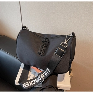 Detail view of black nylon crescent bag with branded wide strap on book background