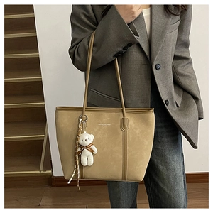 Detail of khaki suede tote bag with plush bear charm and ribbon on model's shoulder