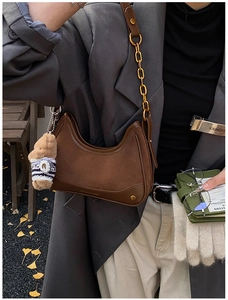 Detail of dark brown suede and leather hobo bag with a gold chain and bear charm