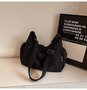 Détail du sac bandoulière en nylon noir avec texture plissée et logo métallique