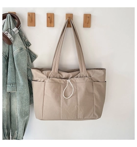 Détail du sac cabas beige avec trois poches avant et cordon de serrage décoratif blanc