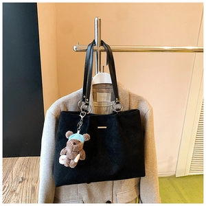 Detail of black quilted tote bag with thin leather straps and a brown plush bear charm