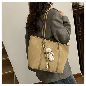 Detailed view of khaki tote bag featuring teddy bear charm and striped scarf accessory
