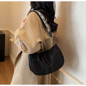 Detailed view of a black half-moon crossbody bag with geometric woven strap on a model