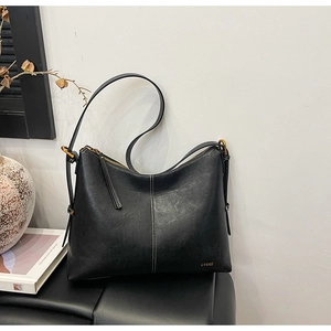 Detail of black leather tote bag with white stitching and gold hardware on a dark stool