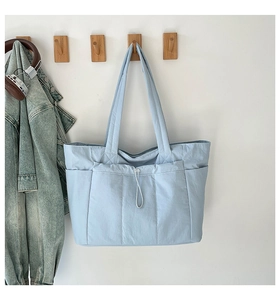 Détail d'un sac cabas bleu clair avec poche avant à cordon suspendu au mur