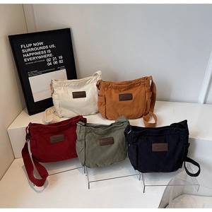 Canvas messenger bags in five colors displayed on white steps with side pocket details