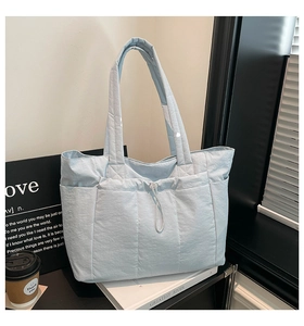 Gros plan du sac cabas matelassé bleu clair montrant la poche latérale et le cordon