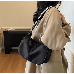 Woman wearing a black canvas crossbody bag with decorative geometric shoulder strap
