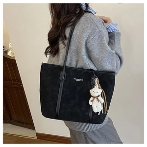 Side view of black matte tote bag with thin straps and cute plush bear charm detail