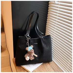 Quilted black tote bag with cute bear charm on wooden surface with soft shadows