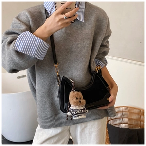 Detail of black half-moon shoulder bag with golden zipper and a cute teddy bear charm
