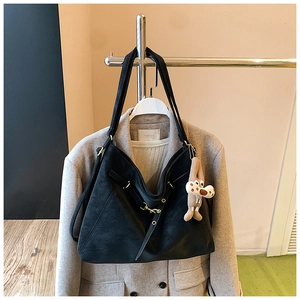 Close-up of black leather tote bag with a cute plush charm and metal buckle details