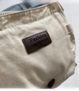 Detail of off-white canvas tote bag featuring brown leather logo patch and stitching