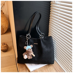 Detail of black quilted tote bag with a small brown teddy bear pendant on wooden ledge