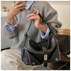 Detail view of black textured leather shoulder bag featuring silver zippers and twist lock