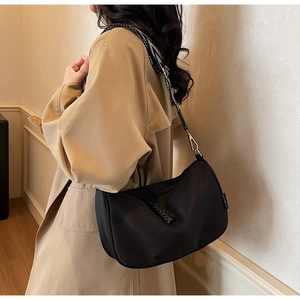 Close-up of black crescent nylon shoulder bag with patterned wide strap on a model