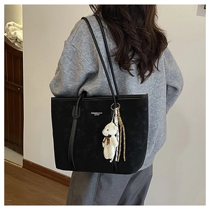 Close-up of black suede tote bag with plush bear charm and striped tassel detail
