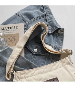 Detail of beige canvas shoulder bag featuring adjustable wide strap and leather logo patch