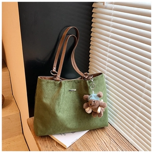 Detail of green quilted tote bag with brown faux leather handles and a bear charm