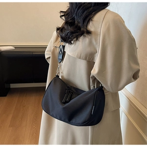Close-up of black nylon crossbody bag featuring a wide geometric pattern strap on beige trench coat