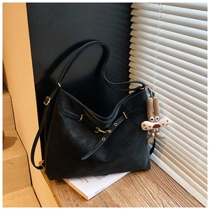 Detail of black matte leather tote bag with metal buckle and plush rabbit charm