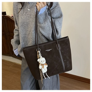 Detail of dark brown suede tote bag with plush bear charm and white printed text
