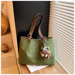 Detail of green tote bag with quilted texture and a cute teddy bear charm on wood
