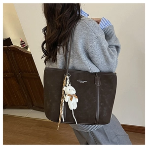 Detail view of the brown frosted tote bag with plush bear charm and white printed text