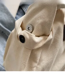 Close-up of silver magnetic clasp on beige canvas tote bag with textured metal finish