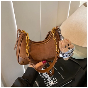 Close-up of brown suede and leather handbag with gold chain and cute plush bear charm
