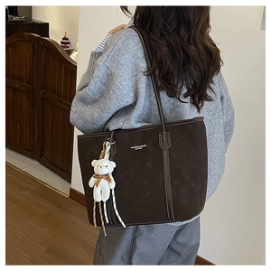 Detail of a dark brown suede tote bag with a plush bear charm on a female model