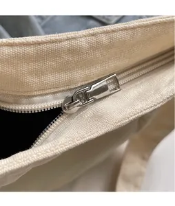 Detail of smooth silver metal zipper head on a minimalist cream canvas shoulder bag