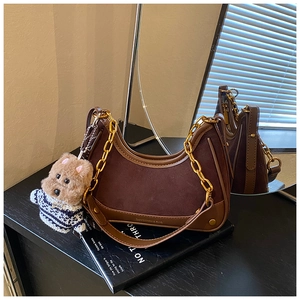 Detail of vintage brown shoulder bag featuring gold chain and cute plush bear charm