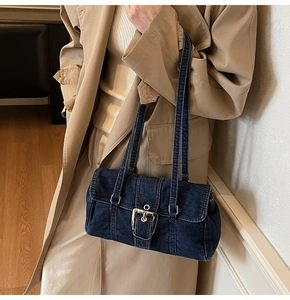Détail du sac à bandoulière en denim bleu foncé avec boucle argentée sur trench beige