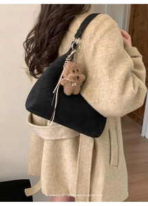 Detalle de bolso tote de ante negro con colgante de osito de peluche y hebilla metálica