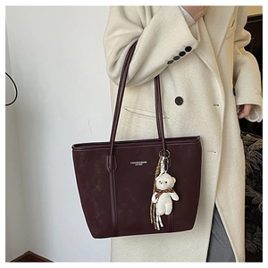 Detail of burgundy leather tote bag featuring a plush white bear charm and shoulder straps