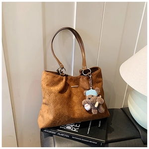 Detail of brown faux suede tote bag with rhombus quilting and a cute teddy bear charm