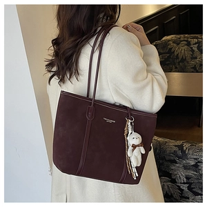 Detail of dark burgundy tote bag with leather texture and cute plush bear charm accessory
