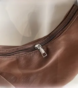 Macro shot of smooth silver metal zipper pull and textured brown leather shoulder bag detail