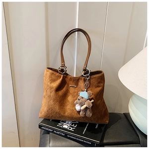 Detail of caramel suede tote bag with woven pattern and a cute teddy bear charm