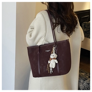 Detail of dark burgundy tote bag with teddy bear pendant on cream coat model