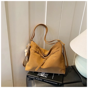 Close-up of caramel leather tote bag with decorative buckle and cute bear charm