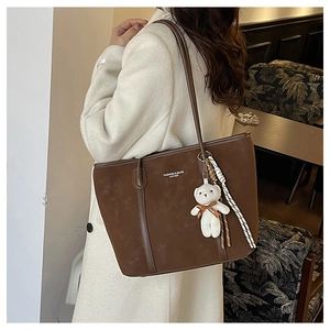 Detail of deep brown leather tote with plush bear charm and fashion text print
