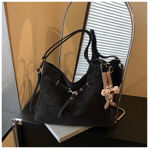 Detail of black matte leather tote bag featuring metal rings and a plush rabbit charm