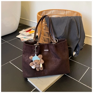 Detail of dark brown tote bag with quilted pattern and a cute bear plush charm on books
